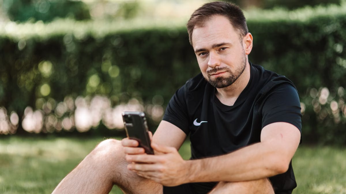 Man in black shirt sitting on grass using a smartphone outdoors.